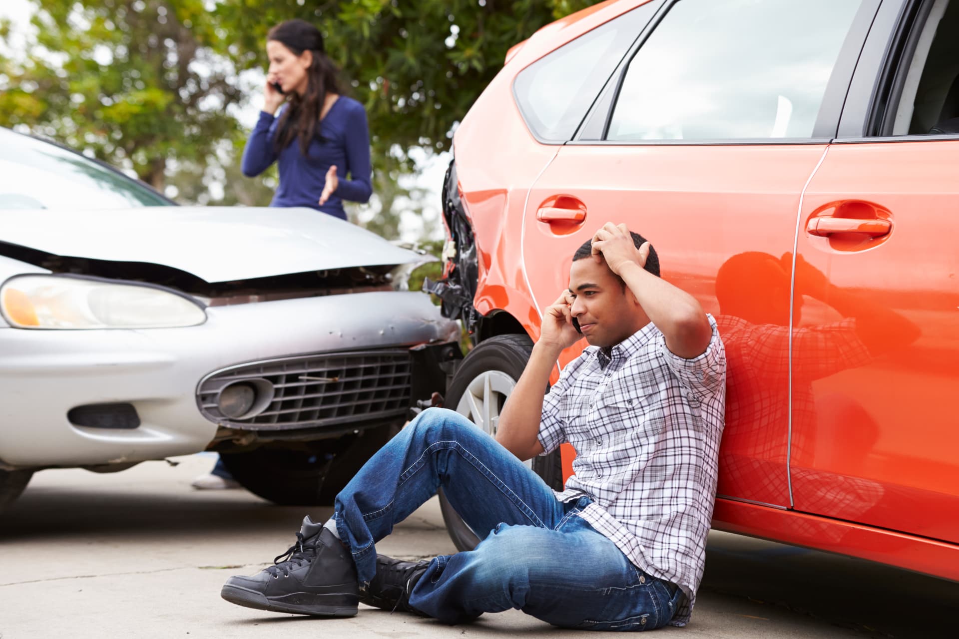 Distressed driver sitting on the ground beside his damaged car after an Ohio accident, making a phone call